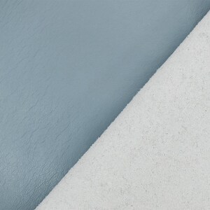 May include: Close-up of two pieces of material. One is a textured, light blue leather, and the other is a white, suede-like fabric. The fabrics are angled against each other, showcasing their contrasting textures and colors.
