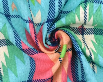 May include: Close-up of a fabric with a colorful geometric pattern. The fabric features a light blue background with a plaid design in dark blue. The pattern includes pink, green, and peach-colored geometric shapes. The fabric is tightly folded.