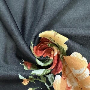 May include: Close-up of black fabric with a floral pattern. The design features large, colorful flowers in shades of red, orange, and yellow, contrasted against a dark background. The fabric is folded, showing the texture and detail of the print.
