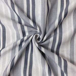 May include: A fabric featuring a pattern of vertical stripes in dark charcoal gray and white. The material is gathered in a central swirl, creating folds that radiate outward and highlight the alternating thick and thin stripe design.
