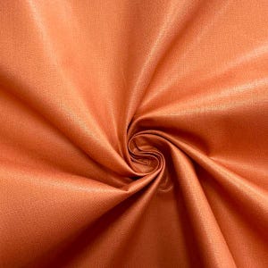 May include: Close-up of a folded, orange fabric with a satin sheen. The fabric is a solid color, with a slight variation in tone due to the folds and shadows. The material appears smooth and luxurious, suitable for apparel or home decor.