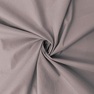May include: A close-up shot of a fabric with a swirling pattern. The fabric is a solid, muted mauve color, with subtle texture visible throughout. The fabric is gathered in the center, creating a spiral effect.