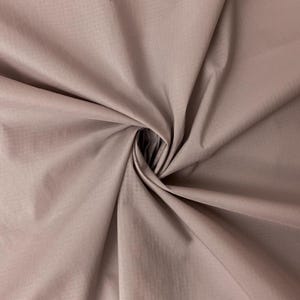May include: Close-up of a dusty rose fabric with a subtle sheen. The material is gathered in a spiral, creating soft folds and shadows. The fabric appears lightweight and smooth, suitable for apparel or home decor.