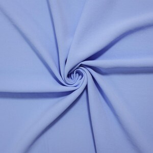 May include: A solid light blue fabric with a smooth, matte texture. The material is gathered in the center, creating soft, radiating folds and drapes that extend outward toward the edges, showcasing the consistent color and even surface.
