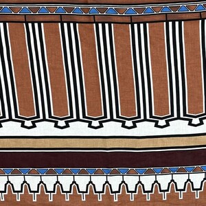 May include: A close-up of a fabric with a repeating geometric pattern. The design features vertical brown and white stripes, accented with black lines. The top and bottom borders have blue triangles and white shapes.