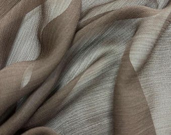 May include: Close-up of a flowing fabric with a striped pattern. The fabric has a sheer quality, with shades of brown and gray creating a layered effect. The light catches the folds, highlighting the texture.