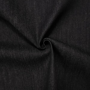 May include: Close-up of black denim fabric with a subtle texture. The fabric is folded and swirled, creating shadows and highlighting the weave. The dark color suggests a versatile material suitable for various clothing items.