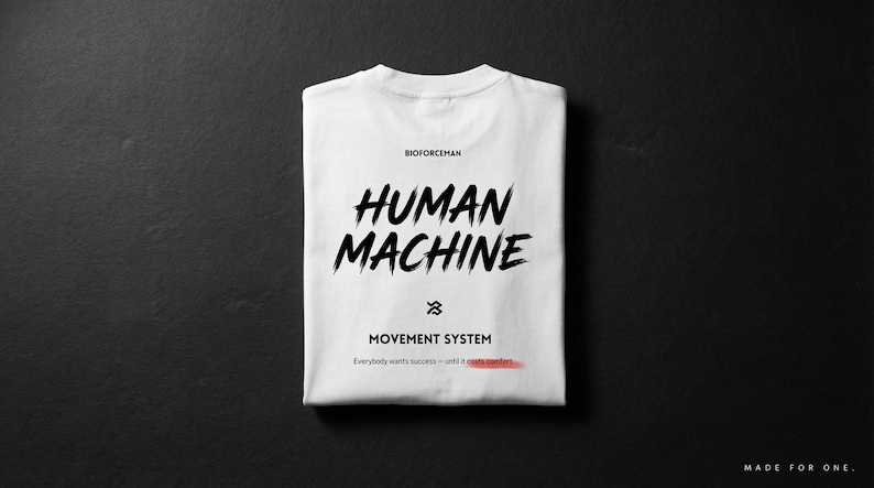 K&ouml;nnte beinhalten: Gefaltetes wei&szlig;es T-Shirt mit dem Schriftzug "HUMAN MACHINE" in schwarzer Pinselstrich-Schrift. Darunter stehen die Worte "MOVEMENT SYSTEM" und der Satz "Everybody wants success - until it costs comfort." Das T-Shirt liegt auf schwarzem Hintergrund.