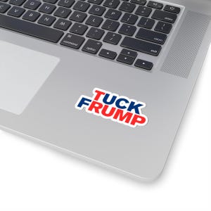May include: A white sticker with the text "TUCK FRUMP" in red and blue, placed on a silver laptop. The sticker's text is outlined in white.