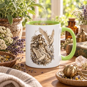 May include: A white ceramic mug with a light green interior and handle, featuring a detailed illustration of a long-haired figure in flowing robes surrounded by two white swans and tall grasses, set against a clean white background.