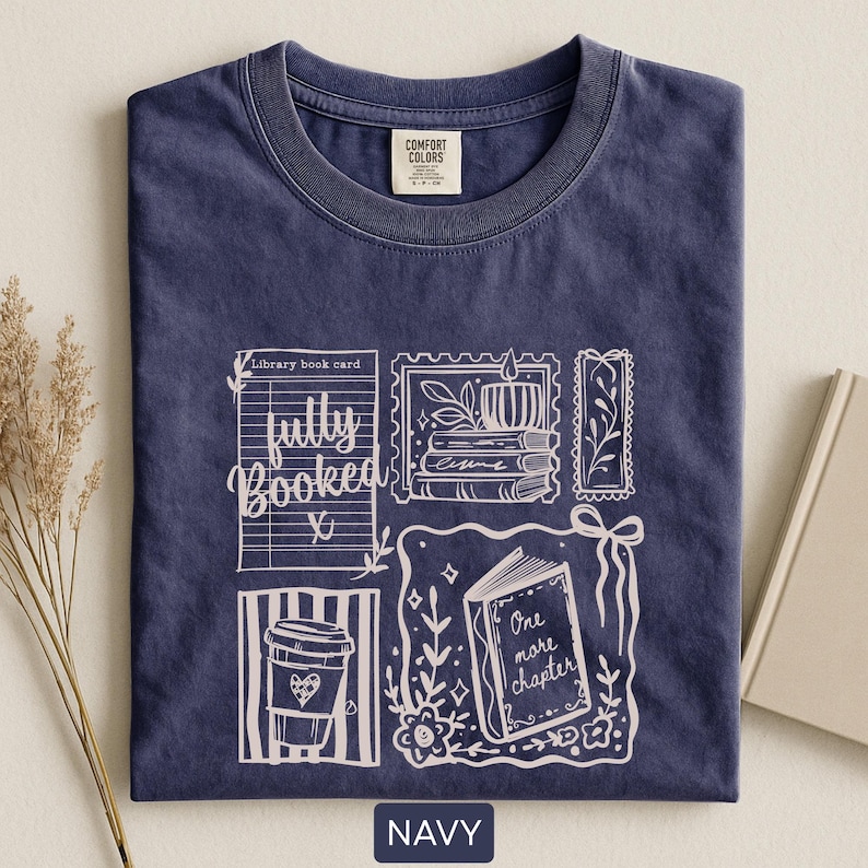 May include: Navy blue t-shirt with a white graphic design featuring a library book card, coffee cup, and an open book with the words "One more chapter." The shirt also has the words "fully booked."