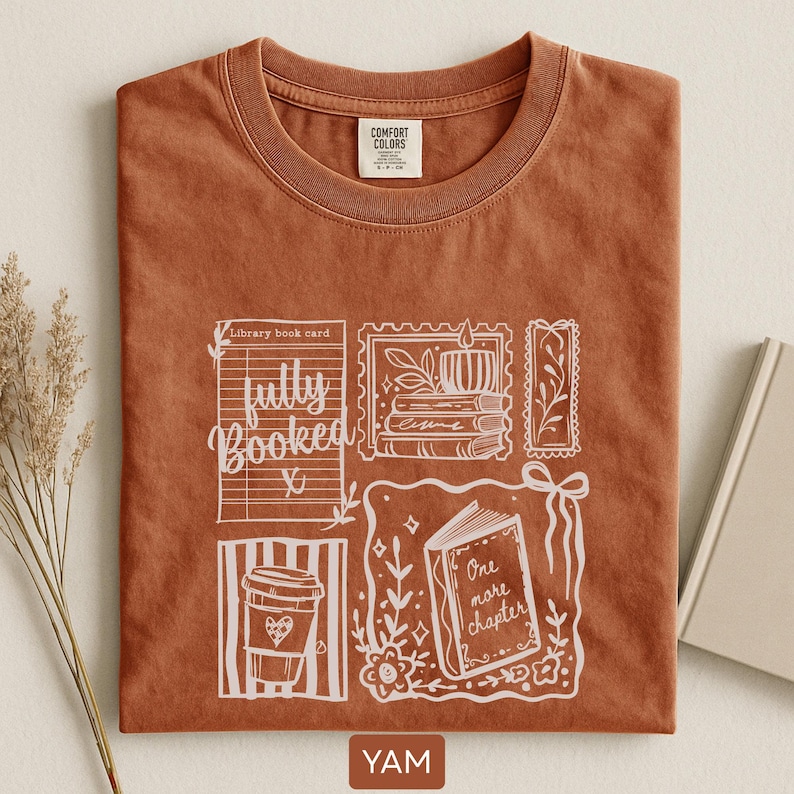May include: A terracotta-coloured t-shirt with a white graphic design featuring a coffee cup, a library book card, and an open book with the words "One more chapter." The shirt also has the text "fully booked."