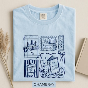 May include: Pale blue t-shirt with a navy blue graphic design including a coffee cup, open book, and the phrases "fully booked" and "one more chapter." The word "Chambray" is printed at the bottom.