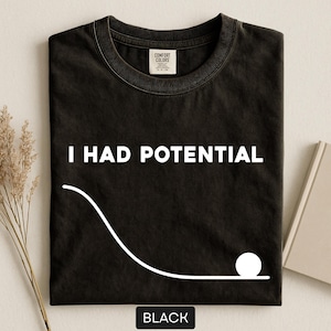 May include: Black t-shirt with the phrase "I HAD POTENTIAL" in white, along with a white graphic of a ball rolling down a curve. The word "BLACK" is at the bottom. The shirt has a crew neck and a tag.