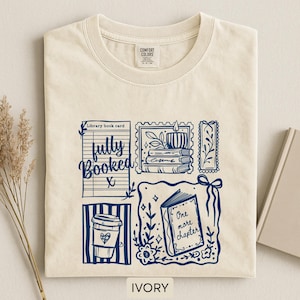 May include: Ivory t-shirt with a navy blue graphic featuring a library book card, coffee cup, candle, and an open book with the words "One more chapter." The shirt also has the words "fully booked."