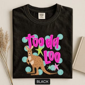 Op de afbeelding: Zwart T-shirt met een kangoeroe-afbeelding en de tekst "Tooda Loo" in roze. Het ontwerp bevat blauwe cirkels en groene en roze sterren. Het T-shirt is gemaakt van een zacht materiaal.