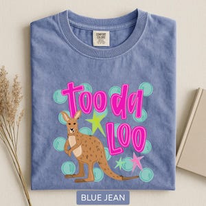 Op de afbeelding: Een blauw spijkerbroekkleurig T-shirt met een kangoeroe-afbeelding. De kangoeroe is bruin met een lichtbruine buik. De tekst "Tooda Loo" is felroze, met groene en roze sterren en turquoise bellen.