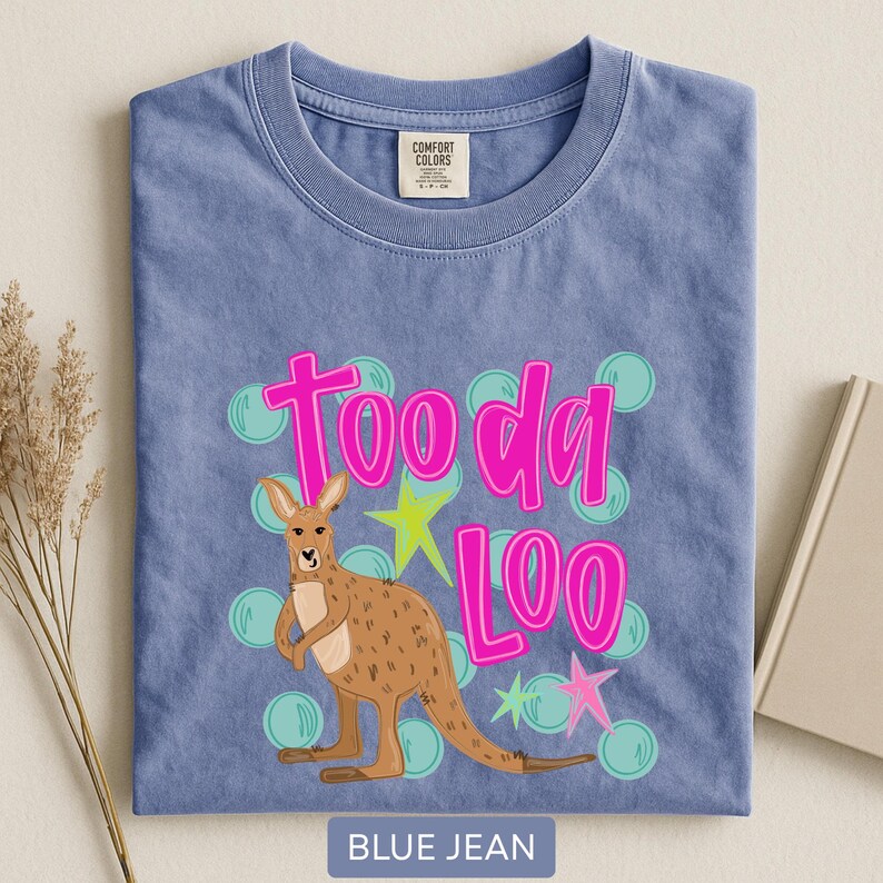 Op de afbeelding: Een blauw spijkerbroekkleurig T-shirt met een kangoeroe-afbeelding. De kangoeroe is bruin met een lichtbruine buik. De tekst "Tooda Loo" is felroze, met groene en roze sterren en turquoise bellen.