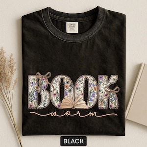 May include: Black t-shirt with the words "BOOK worm" in a floral design. The word "BOOK" is in large letters with a floral pattern, and the word "worm" is in a cursive font. A small open book is between the words.