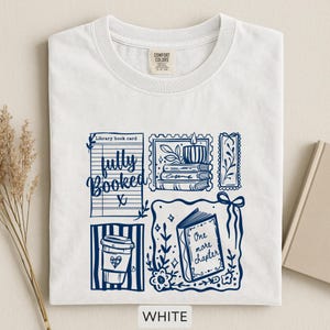 May include: White t-shirt with a navy blue graphic design featuring a coffee cup, open book, and the words "fully booked" and "one more chapter." The shirt has a crew neck and a tag that says "Comfort Colors."