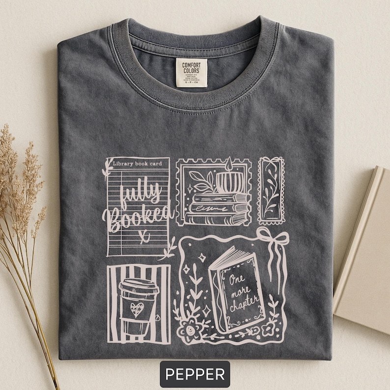 May include: Pepper-coloured t-shirt with a white graphic design featuring a coffee cup, open book, and the words "fully booked" and "one more chapter." The shirt has a crew neck and a Comfort Colors tag.