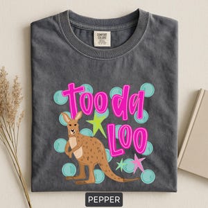 Op de afbeelding: Donkergrijs t-shirt met een kangoeroe-afbeelding en de woorden "Tooda Loo" in felroze. Het ontwerp bevat lichtblauwe bellen en groene en roze sterren. Het shirt is onderaan voorzien van het label "Pepper".