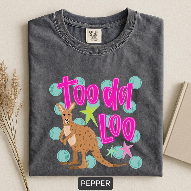 Op de afbeelding: Donkergrijs t-shirt met een kangoeroe-afbeelding en de woorden "Tooda Loo" in felroze. Het ontwerp bevat lichtblauwe bellen en groene en roze sterren. Het shirt is onderaan voorzien van het label "Pepper".