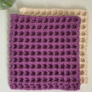 May include: Two handmade crochet washcloths. One is a vibrant purple, and the other is a soft beige. Both have a waffle-stitch pattern. The words "PDF pattern only" are printed at the bottom of the image.