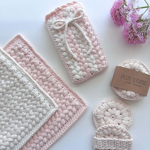 May include: A set of crocheted items including a rectangular pouch with a white bow, two square washcloths in cream and light pink, and three round facial scrubbies. One scrubbie has a brown paper band labeled FACIAL SCRUBBIES 100% COTTON.