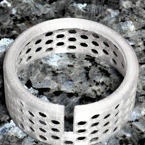 May include: A white, open-design ring with a series of oval-shaped holes. The ring is made of a translucent material and has a smooth, rounded edge. The ring is a decorative item.