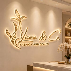 Op de afbeelding: Een goudkleurig, aan de muur gemonteerd 3D-bord met de tekst Liceria & Co. FASHION AND BEAUTY. Het logo bevat een gestileerd lijnprofiel van een gezicht geïntegreerd met bladvormen, allemaal verlicht met een warm, zacht achtergrondlichteffect.