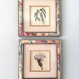 Peut inclure: Deux cadres carrés contenant des illustrations botaniques. Le cadre supérieur présente une tige fleurie violette, tandis que le cadre inférieur montre une orchidée blanche et violette. Les cadres ont une bordure à motifs floraux et un passe-partout rose pâle.