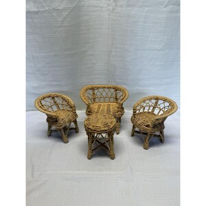May include: A miniature furniture set consisting of two small woven wicker chairs with rounded backs and a matching circular wicker side table. The pieces are crafted from light tan natural reed material with an open lattice design.