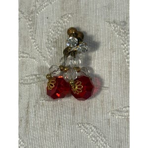 May include: A pair of clip-on earrings featuring two faceted red glass beads shaped like cherries, accented with clear crystal beads and gold-tone metal filigree caps, suspended from a gold-tone metal post with a clear crystal stone.