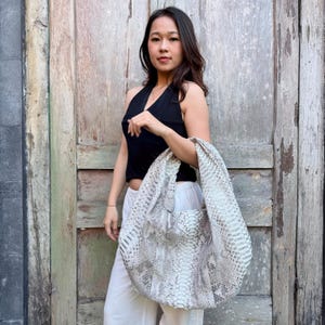 Könnte beinhalten: Eine große, lässige Schultertasche im Hobo-Stil mit einem strukturierten Schlangenledermuster in Off-White und Grau. Die Tasche verfügt über einen breiten, integrierten Riemen, der eine durchgehende Silhouette mit dem Hauptteil bildet und eine weiche Form.