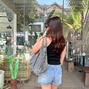 May include: A gray snakeskin-patterned hobo bag with a slouchy silhouette and dual shoulder straps, worn over the shoulder. The bag features a textured, reptilian-inspired print in shades of charcoal and silver, with a spacious, unstructured design.