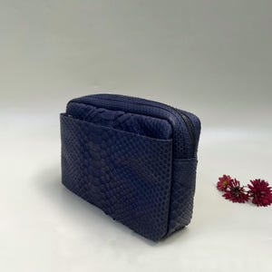Op de afbeelding: Een rechthoekige marineblauwe clutch met een gestructureerd slangenleerpatroon. De tas heeft een hoofdvak met ritssluiting en een extern steekvak aan de voorzijde. Het oppervlak van de tas vertoont een duidelijke schubachtige textuur.