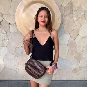 May include: A dark brown crossbody bag with a textured snakeskin pattern, featuring a rectangular shape, a front flap closure, and an adjustable shoulder strap. The bag is worn across the body, resting at the hip, and is made of a glossy material.