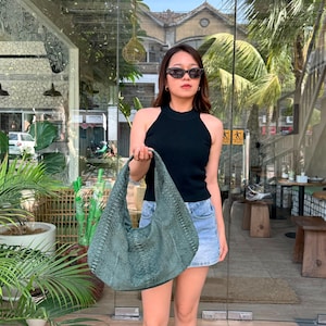 May include: A large, slouchy hobo-style shoulder bag crafted from dark green snakeskin-textured material. The bag features a wide, integrated strap and a curved, crescent-shaped silhouette with a visible scale pattern throughout the exterior surface.