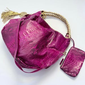 May include: A vibrant magenta hobo bag with a snakeskin-like texture, featuring a braided gold-tone handle, a long matching shoulder strap, and a decorative gold tassel. A small, rectangular matching pouch is attached to the side of the bag.