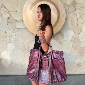 May include: A large, structured handbag crafted from textured, deep magenta snakeskin leather. The bag features two rounded top handles, a gathered design at the top, and a spacious main compartment with visible scale patterns throughout the exterior.