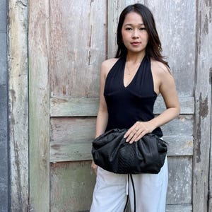 May include: A black clutch bag with a textured snakeskin pattern and a gathered, pouch-like silhouette. The bag features a soft, rounded shape with a frame closure, crafted from a dark material that displays a detailed, scaly surface texture throughout.