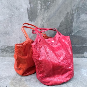 May include: Two tote bags featuring a textured snakeskin pattern. One bag is a vibrant orange, while the other is a bright pink. Both bags have dual top handles and a spacious, open-top design with a structured base and a glossy finish.