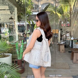 May include: A large, slouchy tote bag featuring a textured, light-colored snakeskin pattern. The bag has a wide shoulder strap and a decorative tassel hanging from the side. It is worn over the shoulder, paired with a black top and denim shorts.