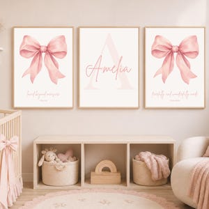 Puede incluir: Tres láminas decorativas enmarcadas con un lazo rosa en acuarela en los cuadros izquierdo y derecho, y el nombre Amelia en letra cursiva sobre una letra A grande en el centro. El cuadro de la izquierda incluye el texto loved beyond measure.