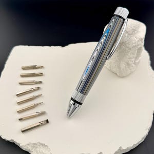 May include: A multi-bit screwdriver with a patterned barrel in shades of blue, grey, and silver. The screwdriver is accompanied by a set of interchangeable bits. The design features a silver clip and a textured grip.