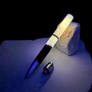 May include: A fountain pen featuring a two-tone design with a solid black lower barrel and a glowing, textured upper cap that emits a bright yellow light. The pen is accompanied by a separate, small, metallic silver cap component.