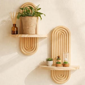 May include: Two wooden wall shelves with an arched design. One shelf holds a potted plant and a brown glass bottle with reeds. The other shelf displays a small succulent, a decorative mushroom, and a glass cloche with a plant inside.
