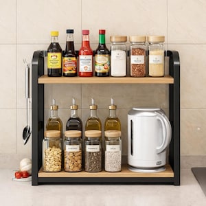 Puede incluir: Un especiero de dos niveles de metal negro y madera lleno de varias botellas y frascos de vidrio. El estante superior contiene botellas de salsas y frascos de sal, pimienta y azúcar. El estante inferior tiene botellas de aceite y frascos de nueces y semillas.