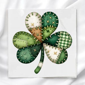 May include: A square image featuring a shamrock design. The shamrock is composed of various green fabric patches, including solid, plaid, and textured patterns, stitched together with contrasting thread. The background is white.